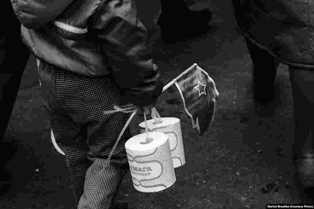 Дзіця нясе рулёны дэфіцытнай туалетнай паперы падчас шэсьця ў гонар Кастрычніцкай рэвалюцыі, 7 лістапада 1988 году 