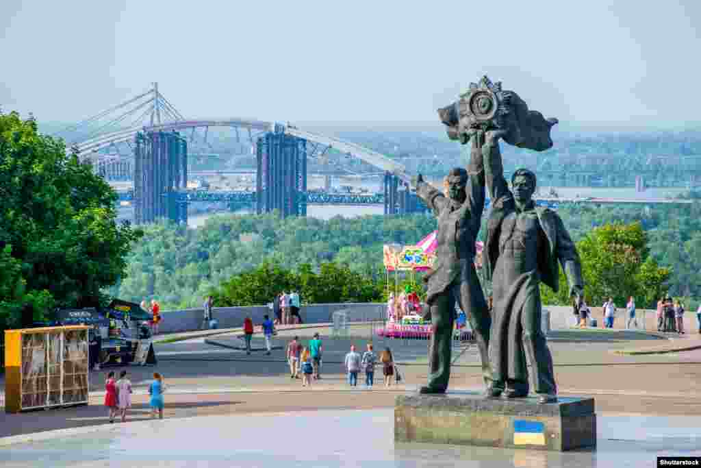 Две центральные фигуры монумента советской эпохи, первоначально называвшегося памятником в честь 300-летия воссоединения Украины с Россией, в центре Киева. Фотография была сделана июне 2018 года. Статуи, изображающие российского и украинского рабочих, объединившихся под советским государственным гербом, были снесены в апреле 2022 года. Месяц спустя комплекс памятников, в который входит большая титановая арка, был переименован в арку Свободы украинского народа 