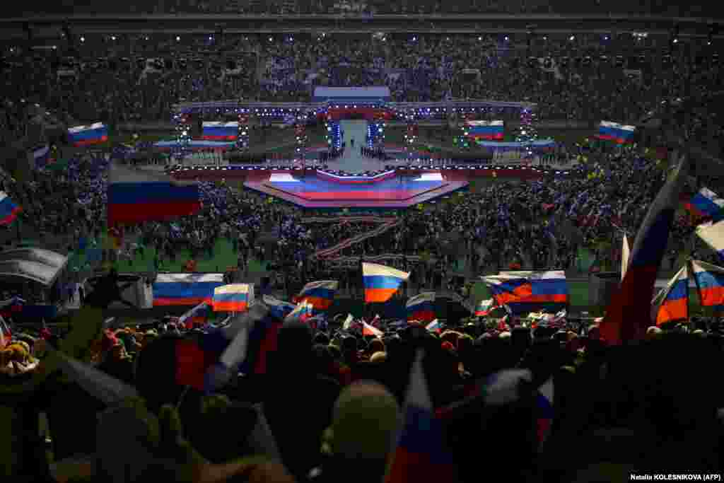 Уладзімір Пуцін выходзіць на сцэну, каб выступіць з прамовай падчас мітынгу-канцэрту, прысьвечанага расейскаму Дню абаронцаў Айчыны, на стадыёне «Лужнікі» ў Маскве. Тады ж журналісты выданьня «Важные истории» даведаліся, што сярод тых, каго выводзілі ў той дзень на сцэну, былі і 15-гадовая Ганна Навуменка і яе малодшая сястра Караліна. Маці дзяўчатак загінула падчас абстрэлу Марыюпалю расейскімі вайскоўцамі ў красавіку 2022 году. Караліна пры выступе закрывала вушы ад моцных гукаў. 22 лютага 2023