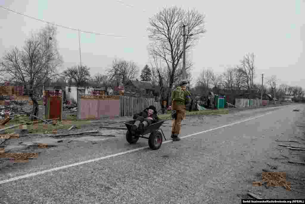 Вмовивши Валентина, військовий і журналісти евакуювали його до безпечного місця, березень 2022 року / Праворуч: та ж вулиця на фото від березня 2024 року. Валентин любив співати й співав нам дорогою до Малина. Після звільнення Київщини дідуся знайшов і забрав до себе його пасинок. Дід Валентин помер. Він помер у мирі, серед своїх близьких. Будинок Валентина вцілів, його зараз ремонтують. Військовий Микита Шандиба продовжує нести службу в ЗСУ