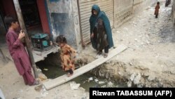 An Afghan girl and her mother cross an open sewer at a refugee camp in Karachi. Pakistan has said that it plans to deport over 1 million Afghans living in the country who do not have valid residency documents.