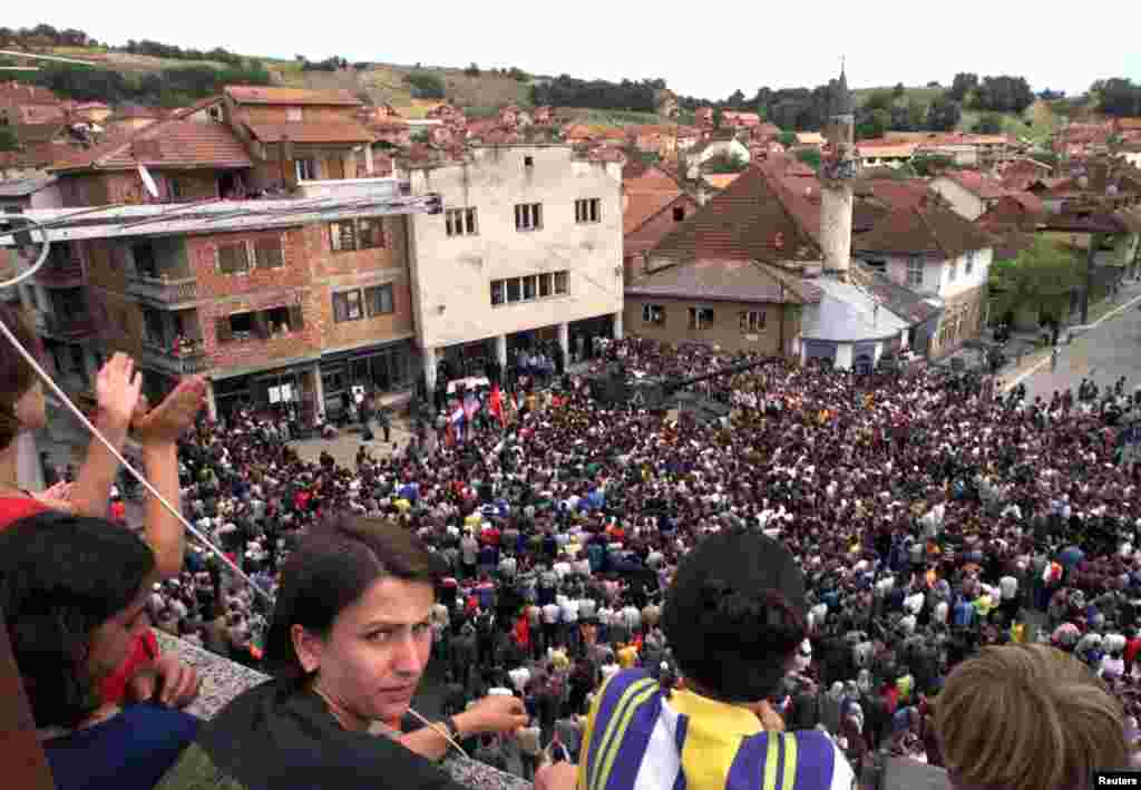 Mii de locuitori de etnie albaneză se adună împotriva posibilei desfășurări a trupelor rusești de menținere a păcii în timpul celei de-a patra zile de proteste din Rahovec, pe 10 iunie 1999. Ei au acuzat că paramilitarii ruși au participat la violențele sârbești împotriva lor. O nouă moschee și copacii plantați recent întâmpină vizitatorii.