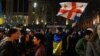 Мъж, увит в украинското знаме, издига флага на Грузия и знамето на ЕС по време на протеста в Тбилиси, Грузия, вечерта на 9 март 2023 г.