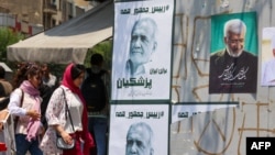 Young women flouting the mandatory Islamic head scarf walk past electoral posters of moderate candidate Masud Pezeshkian (left) and hard-line hopeful Saeed Jalili in Tehran.