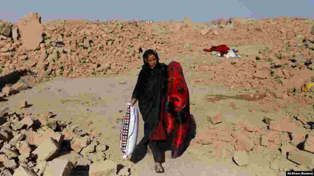  An Afghan woman carries a mattress and pillow that she salvaged from her destroyed home.