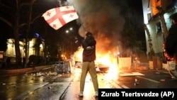 A man waves a Georgian national flag in front of a burning barricade during protests in Tbilisi this week against a controversial 'foreign agent' bill.