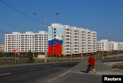 Жінка крокує повз новозведені будинки в Маріуполі