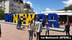 Posetioci festivala iz Srbije i Bosne i Hercegovine ispred spomenika "Newborn" u Prištini. Ove godine je, u znak podrške Ukrajini, u bojama zastave te zemlje. Izmenjen je i redosled slova, uz poruku "No new broken republic", 5. maj 2023.