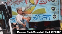 په لواړګي کې یو افغان ماشوم بل کوچنی په غېږ کې نیولی دی او افغانستان ته د تګ لپاره له لارۍ سره نېږدې ولاړ دی - د نومبر لومړۍ انځور.
