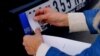 A man placing a sticker on a Serbian car plate to cover Serbian symbols. 