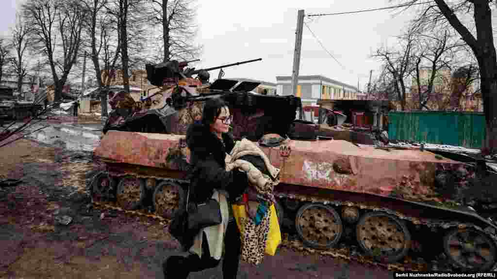 Місцева жителька Ольга: «Коли мій батько будував будинок, побудував під ним кам’яний підвал. І нам заповідав, що «якщо що, то це у вас бомбосховище». Тобто він залив там монолітну плиту. І все. Ми ці слова згадали і, звісно, облаштували там собі – постелили коврики. Спочатку добре почувалися, дивилися телевізор, іноді бігали. Потім, коли це сталося, дивимося: танки почали стріляти уже у нас у дворі. Ми уже капітально побігли у підвал, і там ми сиділи 7 годин. Танки скрипіли гусеницями, був страшний бій, а два танки заховалися за наш дім. Заїжджали до нас у доми. Танки ховалися за будинками, я так розумію. 7 годин цього кошмару: там старі і діти. Ми з життям уже попрощалися, бо над нами так ухало. А потім вийшли і побачили цю страхітливу картину. Як «армагедець» якийсь». Місто Буча, Київська область, 1 березня 2022 року. Праворуч – Ольга у травні 2023 року: «Головне, що всі живі»