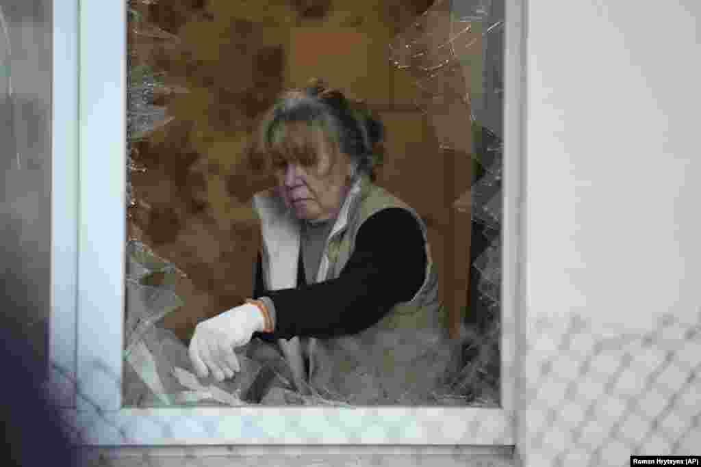 A woman clears broken glass from the window of an apartment building damaged during the attack.