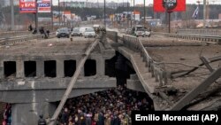 Украински граждани опитват да преминат под съборен от въздушни удари мост в градчето Ирпин на северозапад от Киев. 5 март, 2022.