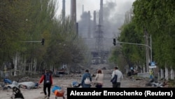 Civilians walk in Ukrainian city of Mariupol as smoke rises from besieged Azovstal steel plant.