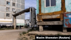 Un bărbat trece pe lângă două clădiri construite pe piloni de beton pentru a preveni scufundarea.