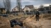 Український військовий біля братської могили з тілами мирних жителів, які, за словами жителів, були вбиті російськими солдатами під час окупації у Бучі, 6 квітня 2022 року