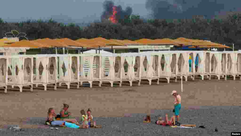 Ljudi se opuštaju na plaži dok se dim i plamen dižu iz ruske vojne vazdušne baze u ukrajinskom okupiranom regionu Krima 9. avgusta 2022. 