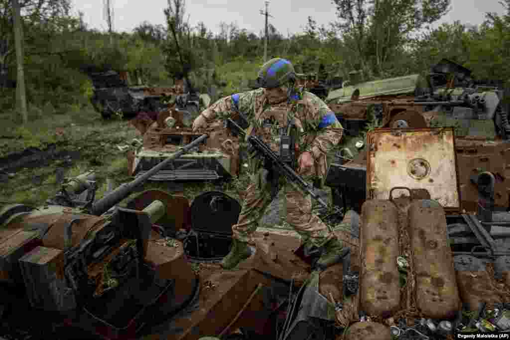 Iuri Usati, un militar al Gărzii Naționale Ucrainene, merge pe APC-urile rusești distruse la punctul de control din apropierea zonei recent recucerite din Izium. Fotografie din 15 septembrie 2022. 