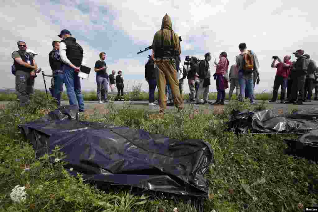 OSCE monitors and journalists look on as a pro-Russian separatist stands guard near bodies taken from a crash site. 