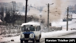 A bus drives past as smoke rises from a building that had been repeatedly hit by tank shells in the southwest of Grozny in January 1995.