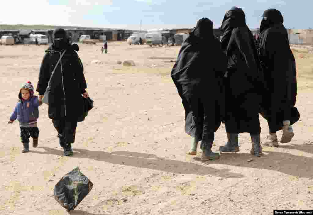 A woman holds hands with a child while walking through al-Hol refugee camp in Syria. 