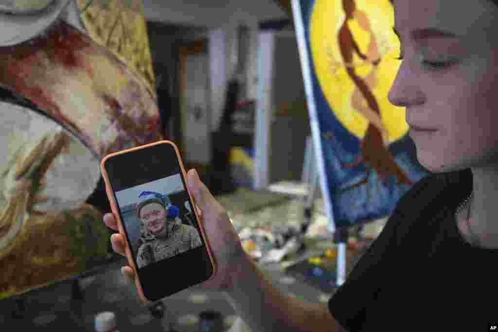 Olesia Skalska arată o fotografie a soțului ei, Roman Skalski, care a fost ucis într-o luptă cu trupele rusești. Ea a venit la studioul de artă cu Irina Farion, pe care a întâlnit-o la un cimitir, un loc în care văduvele ucrainene găsesc consolare una în compania celeilalte și formează prietenii bazate pe durerea comună. În vârstă de 26 de ani, Olesia s-a înrolat voluntar în armată, deși nu avea experiență anterioară de luptă. Cuplul trebuia să sărbătorească prima aniversare a nunții în iunie. Dar, în schimb, Skalska lucrează la un tablou, singurul loc unde pot fi din nou împreună. „Un bărbat duce o fată pe un câmp de grâu care a fost tăiat și îmi imaginez că o poartă astfel încât să nu-și înțepe picioarele”, spune Skalska, în vârstă de 24 de ani, descriindu-și opera de artă.