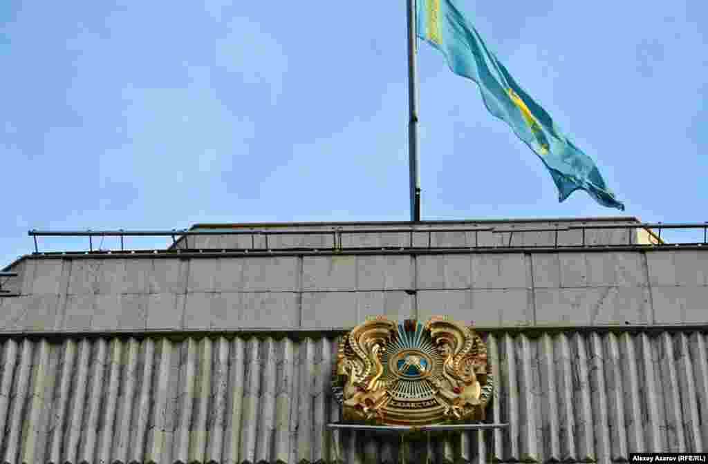 28 июня 2018 года был принят закон о внесении изменений и дополнений в некоторые Конституционные законы Республики Казахстан. В частности, в законе «О государственных символах Республики Казахстан» в статью с описанием герба внесено изменение, касающееся написания страны. Оно должно иметь вид на утвержденной в феврале 2018 года казахской латинице, то есть QAZAQSTAN. Однако, как можно судить по гербам, вывешенным на наружных стенах зданий государственных органов, менять гербы с написанием на кириллице на гербы с латинским написанием не торопились. Данное фото сделано 27 марта 2019 года. Название страны на гербе на здании городского акимата Алматы — еще на кириллице.