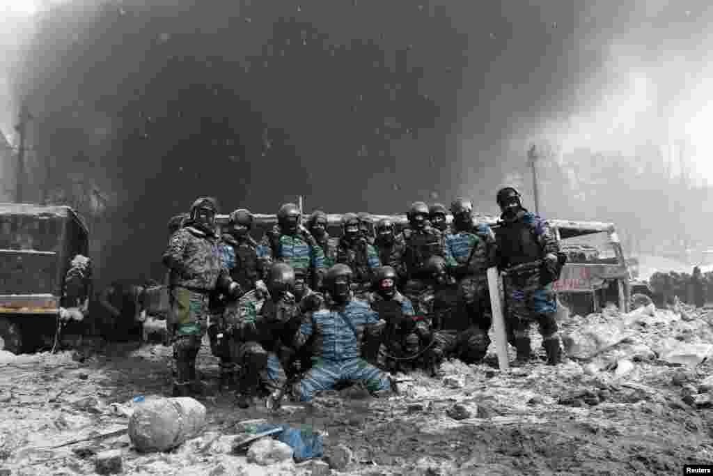 Riot police pose for a picture near a burned-out vehicle.
