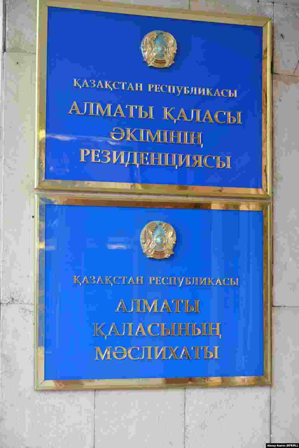 Но если гербов таких больших размеров, как над городским акиматом, в Алматы не так много, то количество подобных табличек с названием государственных учреждений — огромное число (подразделения акимата, школы, детские сады, поликлиники, больницы и так далее). На каждой вывеске — изображение герба. И едва ли все они уже заменены на новые, на которых Казахстан пишется как QAZAQSTAN.