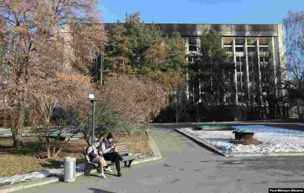 Two people browse on their phones in front of Almaty&#39;s charred city hall on January 12.&nbsp;