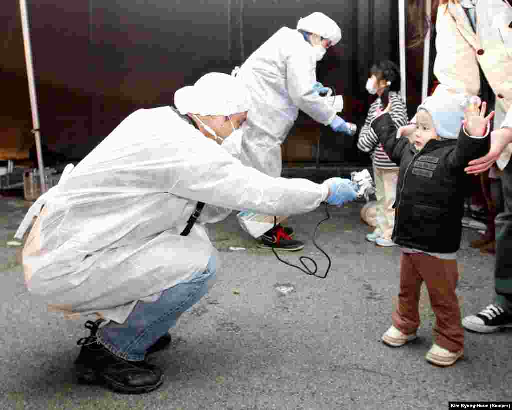 Zvaničnici u zaštitnim odelima proveravaju znakove radiokativnog zračenja na deci koja su evakuisana iz regije u blizini nuklearne elektrane, 13. mart 2011.