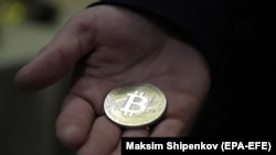 Биткоиндин символикалык тыйынын кармап турган киши.