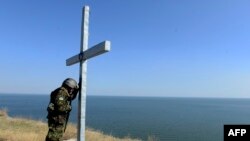 A Ukrainian serviceman prays by a cross outside the eastern city of Mariupol, a port of crucial economic importance on the Azov Sea.