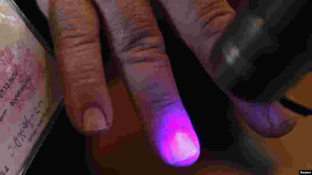 An election official checks a voter's fingers for invisible ink at a polling station in the village of Sartichala.