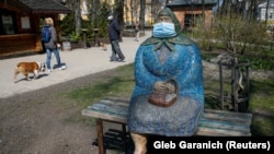 People walk their dogs past a sculpture wearing a protective mask in a park in central Kyiv.
