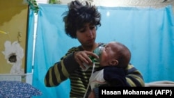 A Syrian boy holds an oxygen mask over the face of an infant at a make-shift hospital following a reported gas attack on the rebel-held town of Douma on the outskirts of the capital, Damascus, on January 22.