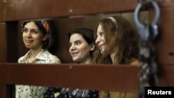 Pussy Riot members Nadezhda Tolokonnikova (from left to right), Yekaterina Samutsevich, and Maria Alyokhina look out from the defendents' cell in a court in Moscow.