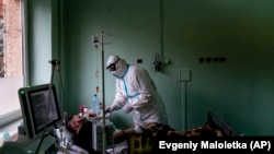 A Ukrainian doctor wearing a special suit to protect against the coronavirus helps a patient with his oxygen mask in the intensive care unit at a regional hospital in Ukraine. (file photo)